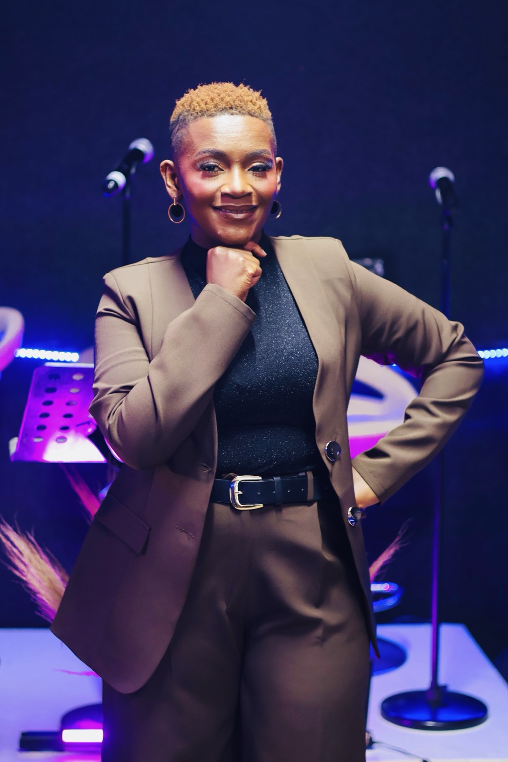 Newie smiling on stage in a brown suit