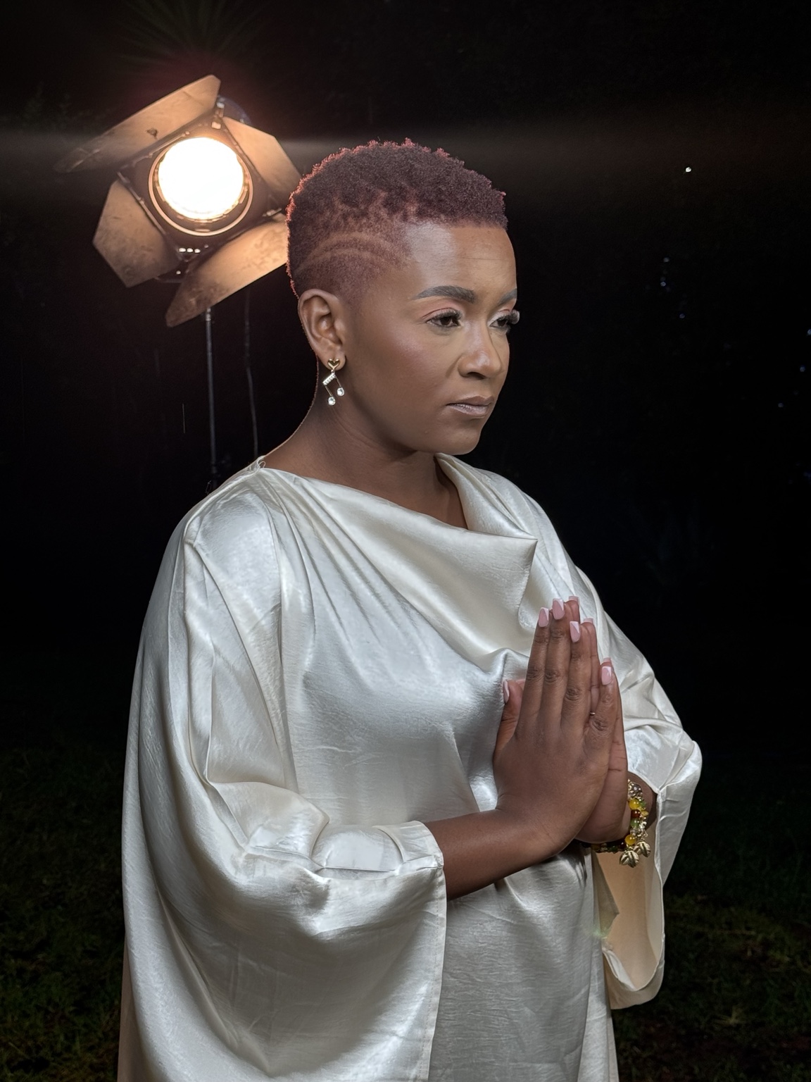 Newie in a silver outfit with her hands together in prayer
